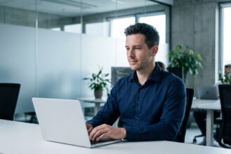 Technicien IT masculin travaillant sereinement sur un ordinateur portable dans un bureau moderne minimaliste, symbolisant la simplification du support informatique